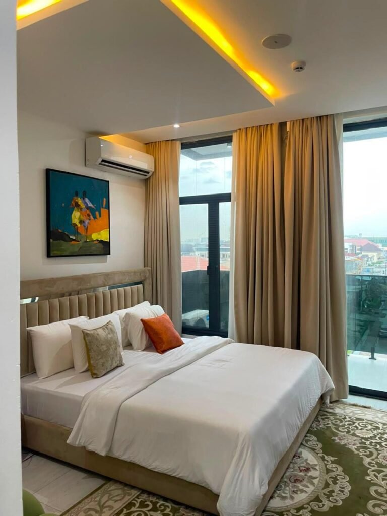 Modern luxury studio apartment bedroom in Lekki with a king-size bed, warm lighting and a city-view balcony